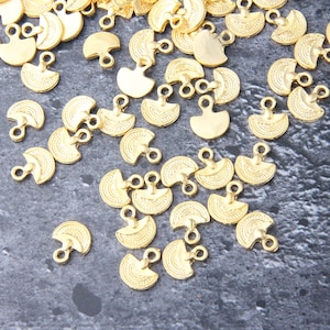 Puede incluir: Una colección de abalorios de metal dorado en forma de semicírculos con detalles decorativos. Cada abalorio tiene dos pequeños bucles para sujetarlo a joyas u otras manualidades.