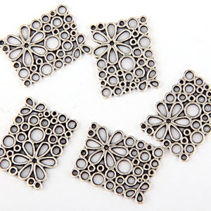 May include: Five silver-toned rectangular metal charms with openwork floral and circular designs. Each charm features a central flower shape surrounded by various sized circles and petal-like shapes. The charms are arranged on a white background.