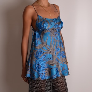 May include: A sleeveless camisole top in a vibrant blue hue featuring a detailed tan and brown swirling floral pattern. The garment has thin spaghetti straps, a scoop neckline, and a relaxed, flowing silhouette that extends to the hips.