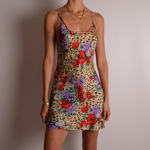 May include: A sleeveless mini dress featuring a tan leopard print background overlaid with a vibrant floral pattern of red and purple flowers. The dress has thin spaghetti straps and a scoop neckline, falling to a short length above the knees.