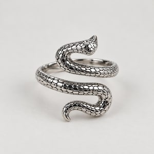 Peut inclure: Une bague en métal argenté en forme de serpent enroulé. L'anneau présente un motif d'écailles texturé et détaillé sur toute sa surface, avec la tête du serpent positionnée à une extrémité et la queue effilée courbée à l'autre extrémité.