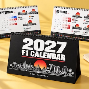 May include: A black 2027 F1 desk calendar with white text and a red sun graphic above a white city skyline illustration. Two additional calendar pages for September and October are visible in the background, displaying monthly grids and race locations.