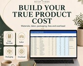 A laptop displays a product cost component builder spreadsheet next to a notebook, mug, and small plant.