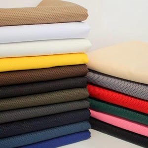 May include: A stack of folded fabric sheets in various colors including beige, white, cream, yellow, brown, black, olive, gray, navy, and blue. Each piece of fabric features a fine, uniform dotted texture across the entire surface area.