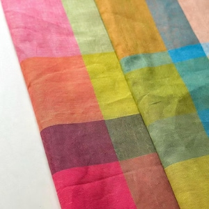 May include: A textile fabric featuring a vibrant grid pattern composed of multicolored squares. The design includes shades of hot pink, orange, lime green, olive, teal, light blue, and yellow, arranged in a repeating block layout with a visible weave.