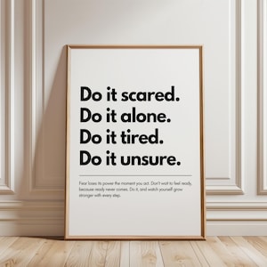 May include: A rectangular wall art print in a light wood frame featuring black text on a white background. The text reads: Do it scared. Do it alone. Do it tired. Do it unsure. Below this, smaller text reads: Fear loses its power the moment you act.