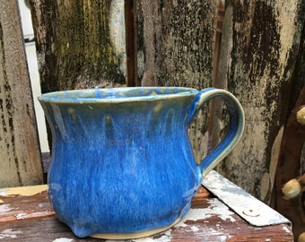 May include: A blue ceramic mug with a light blue glaze and a yellow rim. The mug has a rounded body and a handle.