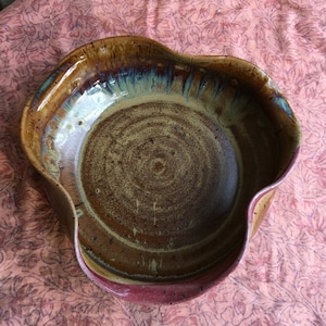 May include: A brown ceramic bowl with a wavy rim and a speckled glaze. The bowl has a deep, round shape and a slightly raised lip.