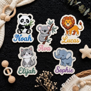 Peut inclure: Cinq autocollants découpés représentant des animaux de dessin animé : un panda avec du bambou nommé Noah, un koala sur une branche nommé Ava, un lion nommé Lucas, un chat gris nommé Elijah et un éléphant nommé Sophie. Bordure blanche.