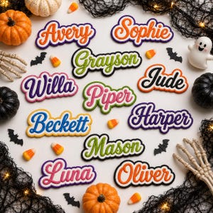 Könnte beinhalten: Eine Sammlung von elf personalisierten Namensaufnähern in verschiedenen Farben und Schreibschriften, angeordnet auf einer weißen Oberfläche mit Halloween-Dekorationen wie kleinen Kürbissen, einer Geisterfigur, Skeletthänden, schwarzen Fledermäusen und Zuckermais.
