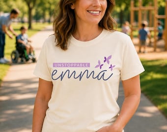 Peut inclure: Un t-shirt à manches courtes de couleur crème avec le texte UNSTOPPABLE dans un rectangle violet au-dessus du mot emma en écriture cursive bleu foncé, accompagné de trois petits papillons violets placés à droite du texte.