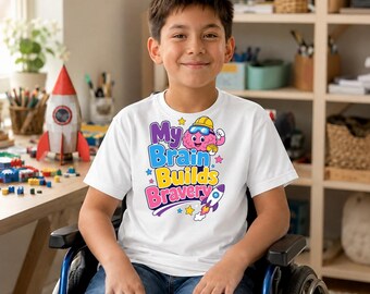 May include: A white short-sleeved t-shirt featuring a colourful graphic print that says My Brain Builds Bravery. The design includes a cartoon brain wearing a yellow hard hat and blue goggles, along with a small rocket ship and colourful stars.