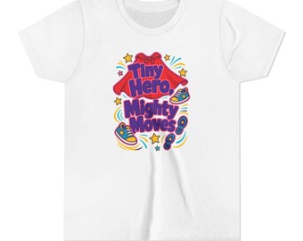 May include: A white short-sleeved t-shirt featuring a graphic print with the text Tiny Hero, Mighty Moves in purple letters. The design includes a red cape, two blue and yellow trainers, yellow stars, and blue footprints on a white background.