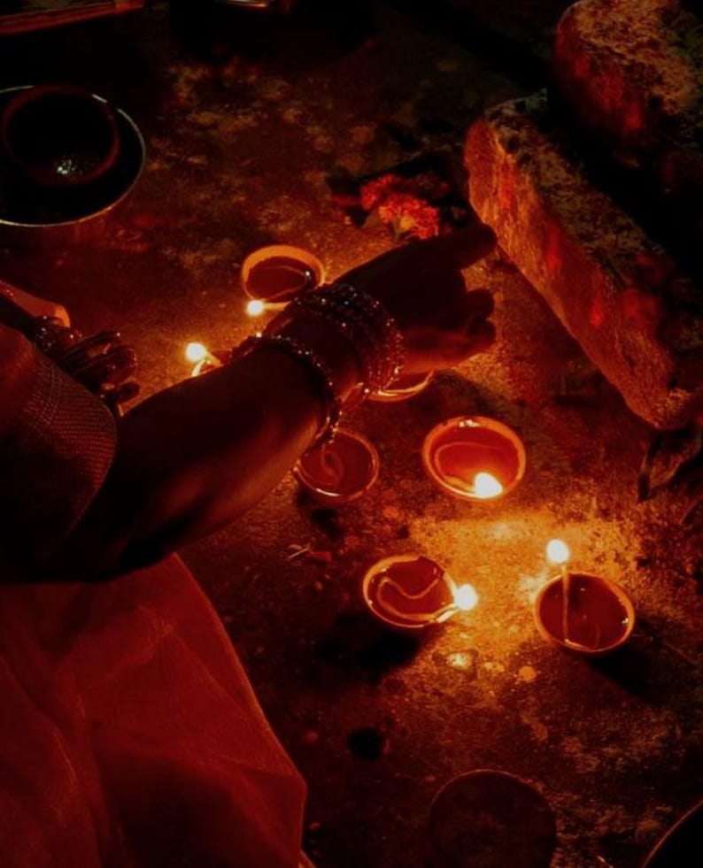 Pode incluir: Uma cole&ccedil;&atilde;o de pequenas l&acirc;mpadas de &oacute;leo redondas de terracota, conhecidas como diyas, est&atilde;o dispostas no ch&atilde;o. Cada l&acirc;mpada cont&eacute;m um pavio aceso que emite um brilho dourado quente, iluminando a &aacute;rea com uma luz suave e cintilante.