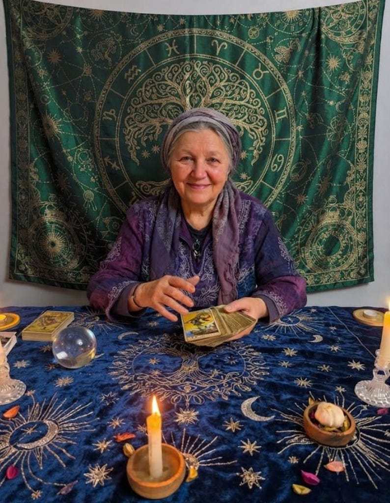 Pode incluir: Uma toalha de mesa de veludo azul-escuro com padr&otilde;es celestiais dourados, incluindo s&oacute;is, luas e estrelas. A mesa est&aacute; disposta com uma bola de cristal transparente, duas velas brancas acesas em suportes de madeira e p&eacute;talas espalhadas.