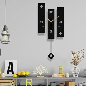 May include: A wall clock featuring three vertical black rectangular panels with silver numerals 12, 3, 6, and 9. The clock has gold-colored hour and minute hands and a central pendulum with a black diamond-shaped weight hanging below the panels.