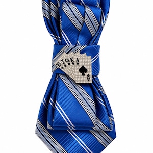 May include: A bright blue necktie featuring diagonal white and silver stripes, secured with a decorative metal clip shaped like a royal flush of playing cards. The card clip is embellished with small clear crystals and displays the letters 10, J, Q, K, A.