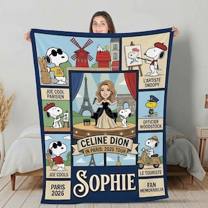 May include: A rectangular fleece blanket featuring a central illustration of a singer on stage with the text Celine Dion In Paris: 2026 Tour and Sophie. Surrounding panels depict Snoopy in various outfits with labels like Joe Cool, L'Artiste, and Le Touriste.