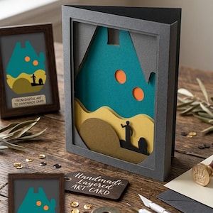 May include: A layered paper art card featuring a dark grey frame with a teal sky, two orange circles, yellow dunes, and a black silhouette of a figure and a droid. The card includes text that reads FROM DIGITAL ART TO HANDMADE CARD.