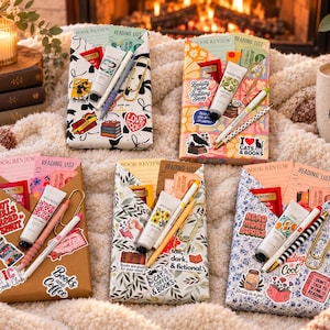 May include: Five rectangular paper envelopes decorated with various stickers, each containing a book review card, a reading list, a tea bag, a small tube of hand cream, a pen, and a large gold paper clip, arranged on a soft textured surface.