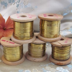 May include: Five spools of gold metallic trim wound on wooden spools. The spools are labeled "Made in France".
