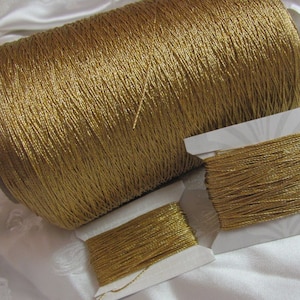 May include: A spool of gold metallic thread, wound on a cardboard tube, with two smaller spools of the same thread.
