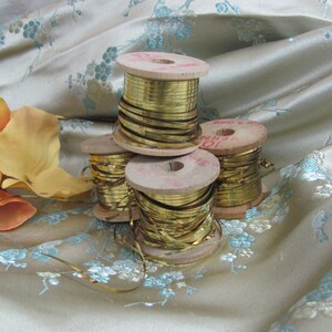 May include: Four spools of gold metallic trim wound on wooden spools. The spools are stacked on top of each other. The trim is shiny and reflective.