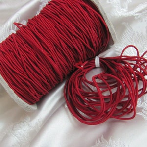 May include: A spool of red elastic cord, wound tightly and ready to be used for crafting projects.