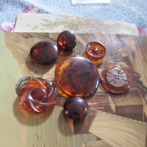 May include: Assortment of eight vintage brown and amber buttons with various designs, including a swirl, a four-hole button, and a button with a silver centre.