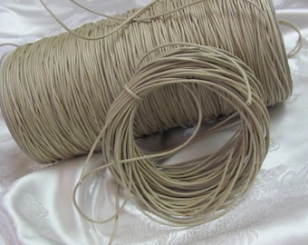 May include: A spool of beige leather cord, wound around itself, with a loose end of the cord hanging off the spool.
