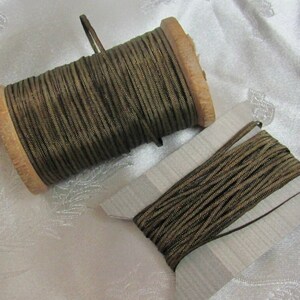 May include: Two spools of brown and gold metallic cord. One spool is on a wooden bobbin and the other is on a cardboard spool.