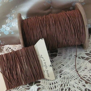 May include: Two spools of brown waxed cord with paper labels. The label on the spool on the right reads "Just a trifle fancier".