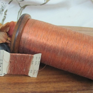 May include: A spool of copper-colored thread wound on a wooden bobbin. The thread is labeled "Dou Dou" and "sa - bots" on a small paper tag.