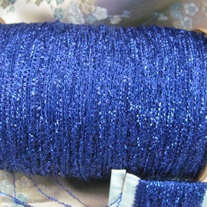 May include: A spool of blue metallic thread with a wooden center. The thread is wound tightly and has a sparkly finish.