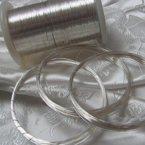 May include: A spool of silver wire with several coils of wire already unwound. The wire is shiny and metallic.