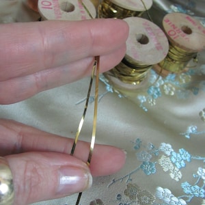 May include: Two spools of gold metallic thread, each with a label that reads "10 yards". The thread is being held by a finger.