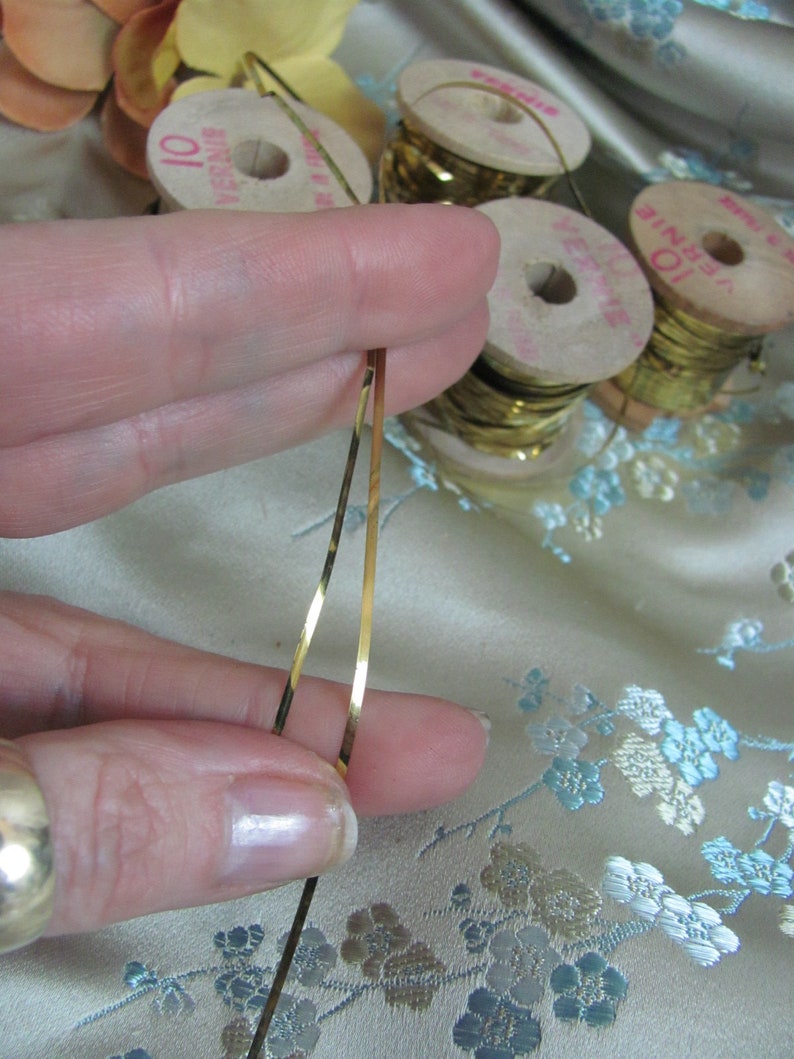 May include: Two spools of gold metallic thread, each with a label that reads "10 yards". The thread is being held by a finger.