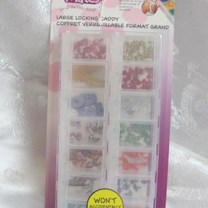May include: A clear plastic storage box with a yellow label that says "Won't Accidentally Open!" The box has 12 compartments filled with various colorful beads, buttons, and other craft supplies. The box is labeled "Craft Mates Large Locking Caddy" and "2 Pack Paquet Double".