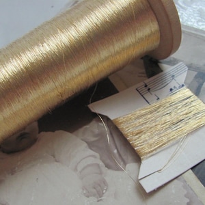 Könnte beinhalten: Eine Spule mit goldenem Metallic-Garn auf einer Holzspule. Das Garn ist um die Spule gewickelt und bereit zum Nähen oder Sticken.
