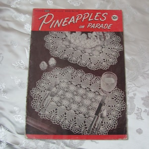 Op de afbeelding: Vintage haakpatroonboekje met een rode omslag en de titel "Ananas in optocht" met een prijskaartje van 10 cent. Het boekje bevat twee afbeeldingen van gehaakte doilies met ananasontwerpen.