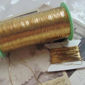 May include: Two spools of gold metallic thread. The larger spool is on a green plastic bobbin and the smaller spool is on a white cardboard bobbin.