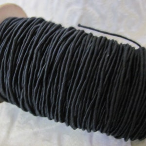 May include: A spool of black elastic cord, wound tightly on a wooden spool.