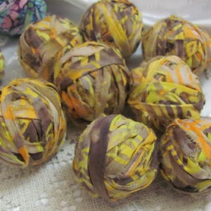 May include: A collection of handmade yarn balls in shades of brown, yellow, and orange. The yarn is wrapped in a spiral pattern, creating a textured and colorful look.