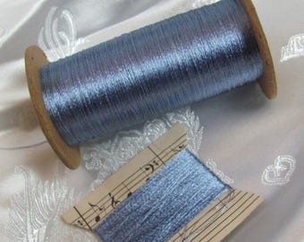 Könnte beinhalten: Eine Spule aus metallisch blauem Garn mit Holzkern und eine kleinere flache Karte, die mit demselben blauen Garn umwickelt ist. Die flache Karte zeigt ein aufgedrucktes Notensystem mit Noten und einem Bassschlüssel auf ihrer Oberfläche.