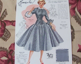 May include: A vintage advertisement for a women's dress featuring a model wearing a blue and white gingham dress with a fitted bodice and a full skirt. The dress is called "Romantic!" and is made with "color-locked Chromspun Tofflo" fabric. The ad also features a close-up of the fabric and the brand name "Fashion Frocks, Cincinnati, Ohio."