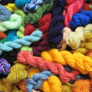 May include: A close-up of a collection of colourful yarn skeins in shades of blue, green, red, yellow, and orange. The image displays a variety of textures and thicknesses, ideal for knitting, crochet, or other fibre art projects.