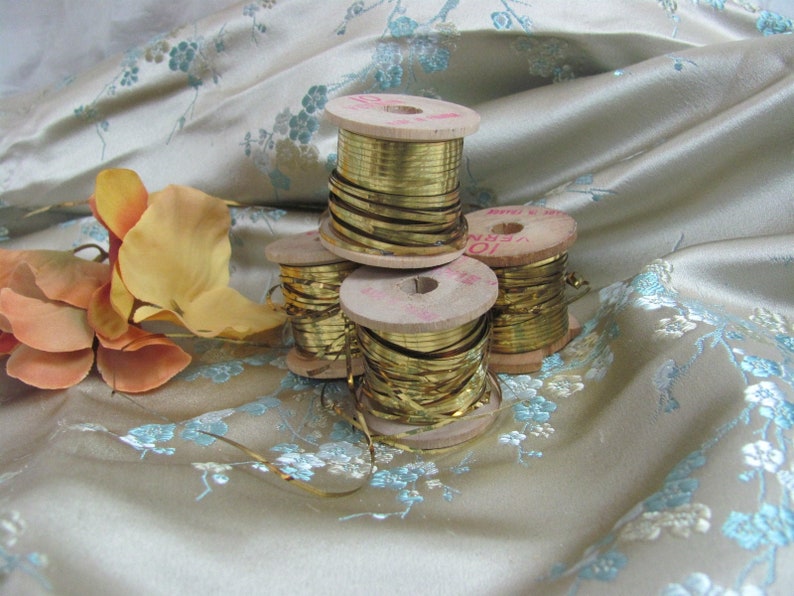 May include: Four spools of gold metallic trim wound on wooden spools. The spools are stacked on top of each other. The trim is shiny and reflective.