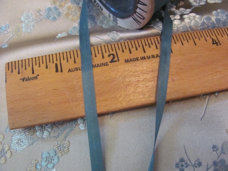 K&ouml;nnte beinhalten: Ein Holzlineal mit den Worten "Falcon", "Auburn Maine" und "Made in U.S.A." darauf gedruckt. Ein dunkelgr&uuml;nes Band liegt auf dem Lineal.