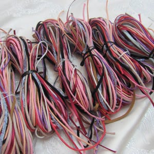 May include: Several bundles of colourful cord in shades of pink, red, black, and white. The cords are tied together with black or clear bands. These cords are likely used for crafts or jewellery making.