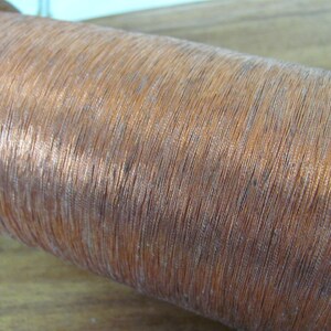 May include: A close-up of a spool of copper wire. The wire is wound tightly around the spool, creating a smooth, shiny surface.
